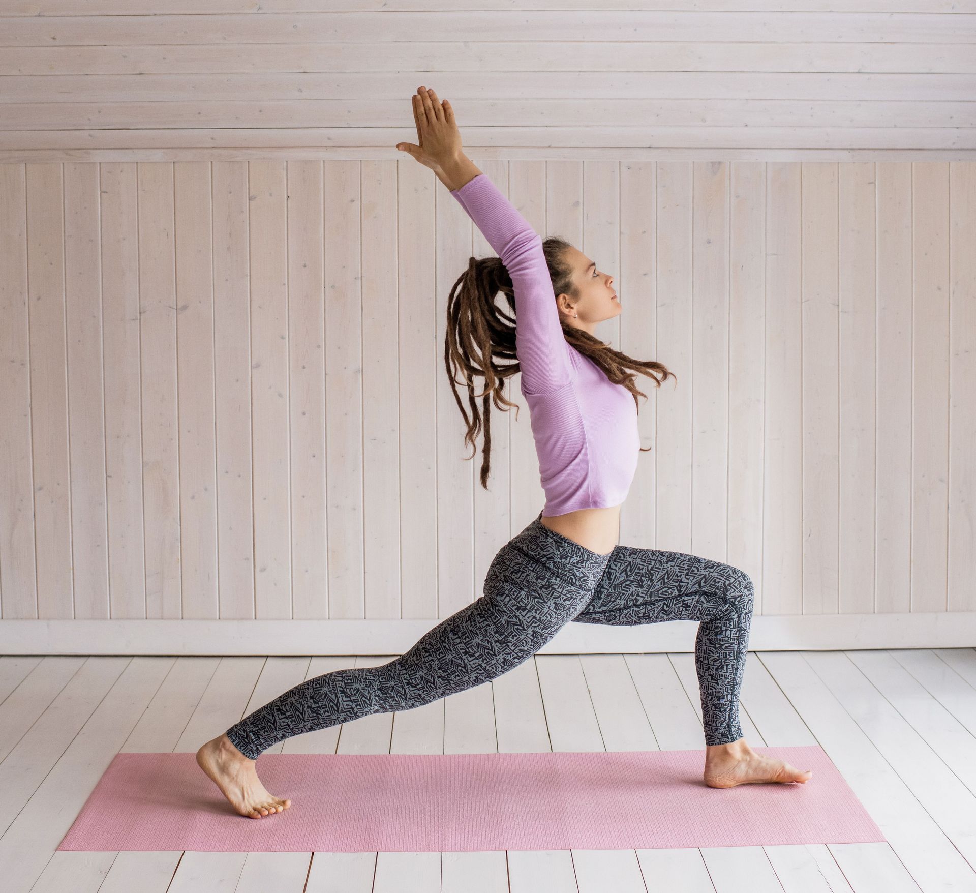 Woman in yoga pose indoors on pink mat wearing activewear.